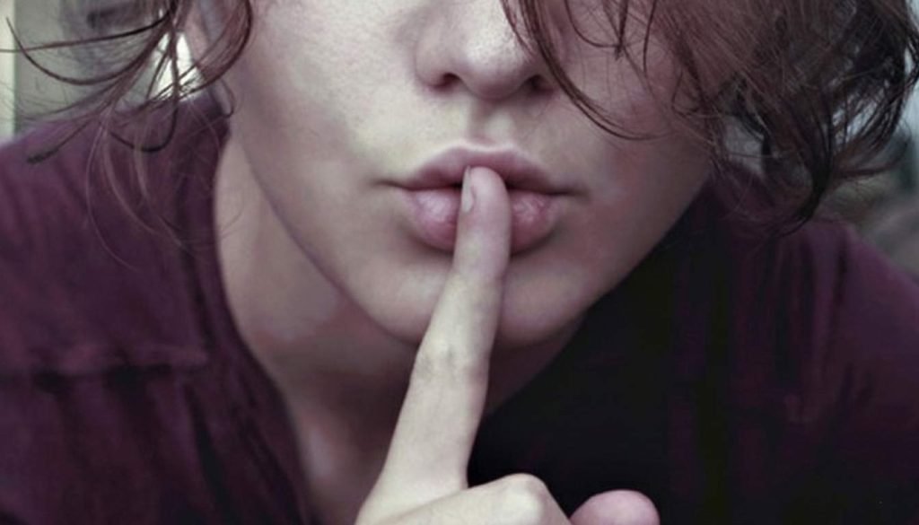 Mujer joven con dedo en los labios haciendo gesto de silencio, representando la reflexión antes de criticar y la pobreza emocional de juzgar constantemente